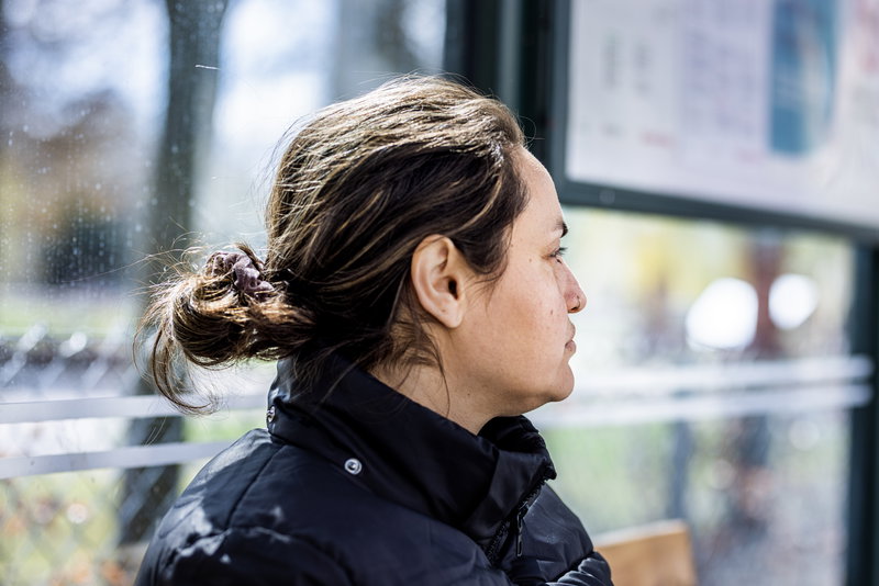 kvinna med uppsatt brunt hår och svart jacka sitter i en busskur