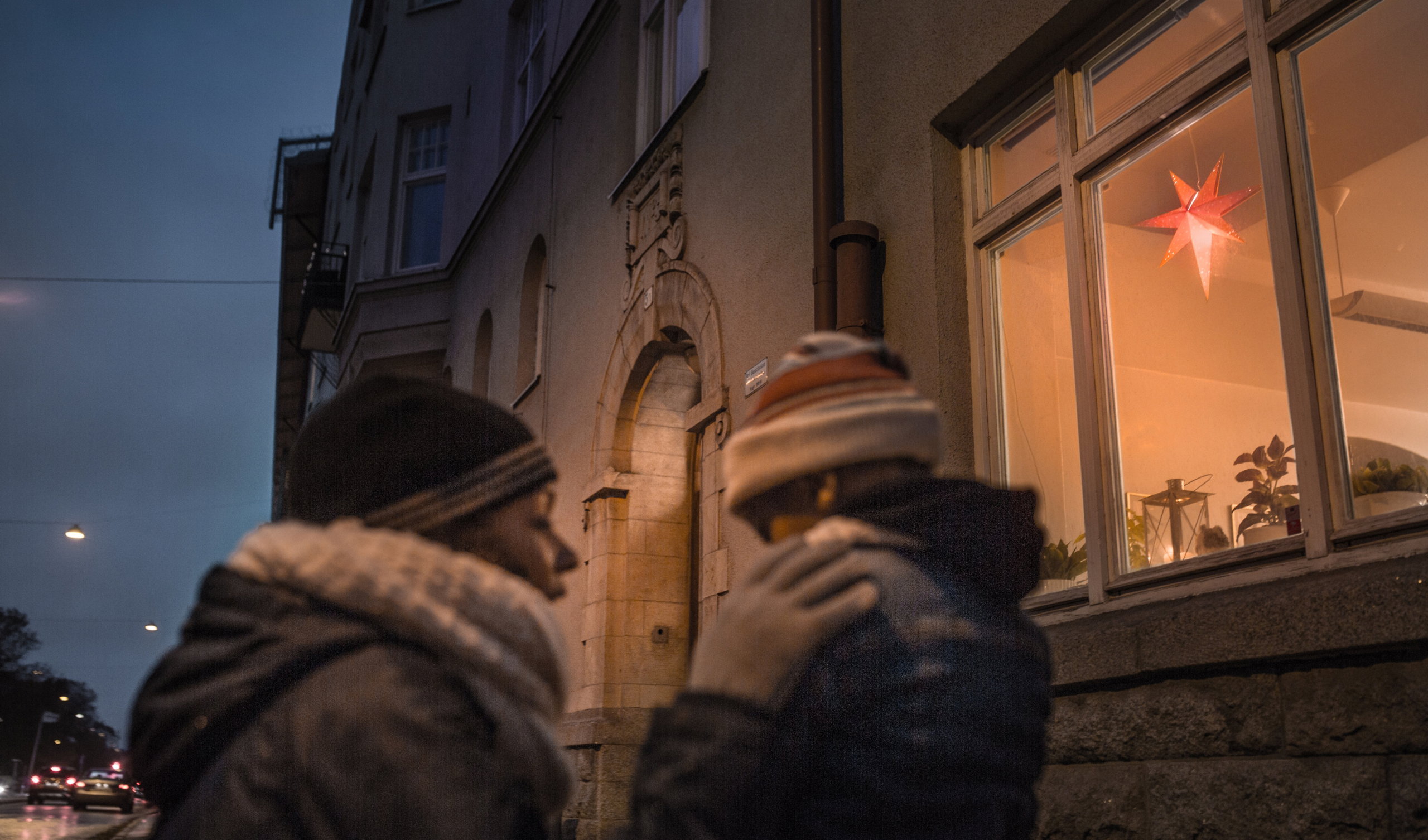 Ensamstående mamma med barn i mörkret utanför en upplyst lägenhet